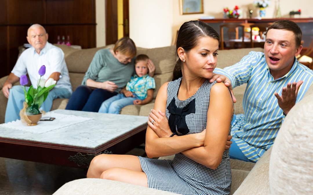 Engaged woman sitting on couch in living room having argument with family members.