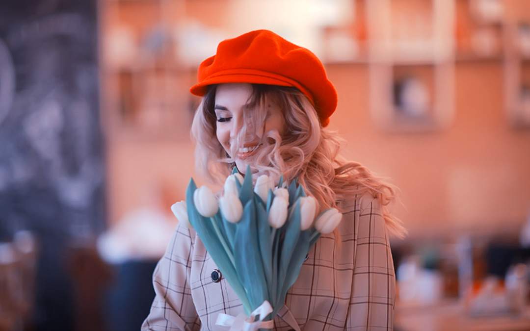 Newly engaged young woman smiling while wearing a red cap and holding a bunch of white tulips.