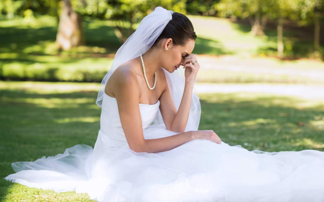 Distressed bride sitting on grass with head in her hands.