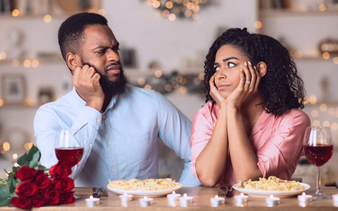 Engaged couple having dinner while looking at each other with disapproval.