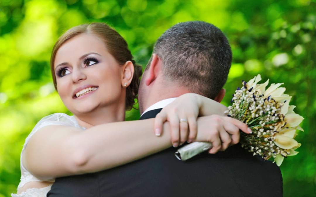 Bride smiling while hugging groom and holding wedding bouquet.