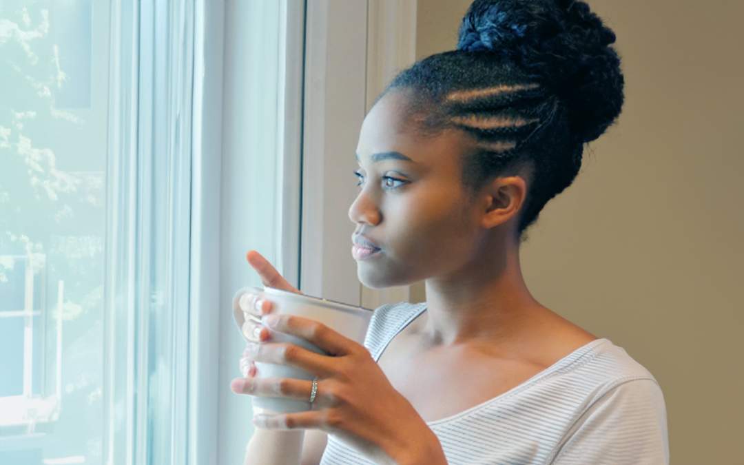 Young engaged woman holding coffee cup and looking pensive while staring out the window.