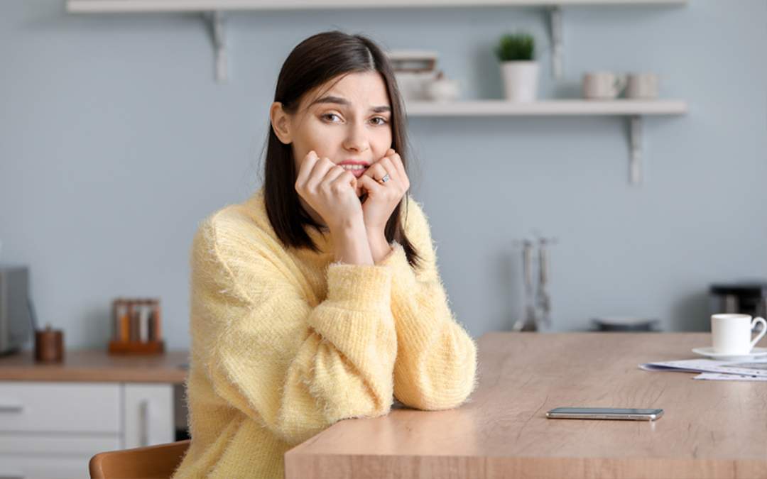 Engaged woman looking extremely anxious and worried while sitting at kitchen table.